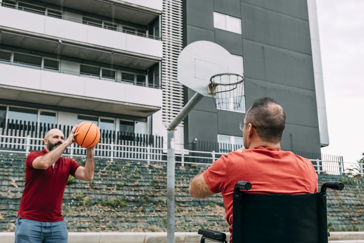 Two men playing wheelchair basketball outdoors.